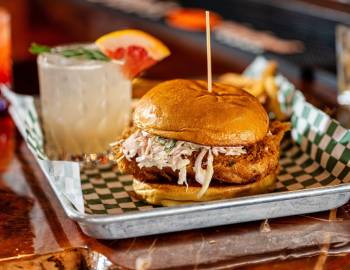 A fried fish sandwich on a tray with a drink