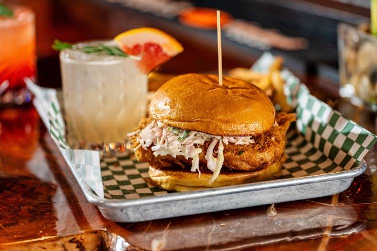 A fried fish sandwich on a tray alongside a drink