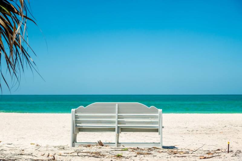 A bench on an empty white-sand beach facing a calm ocean