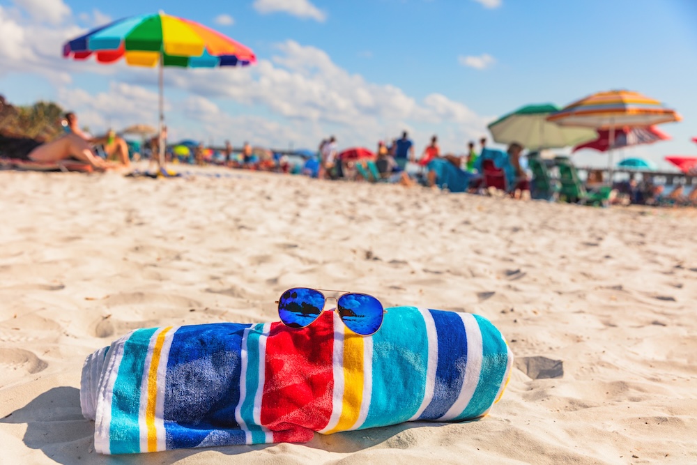 crowded beach with focus on towel and sunglasses 